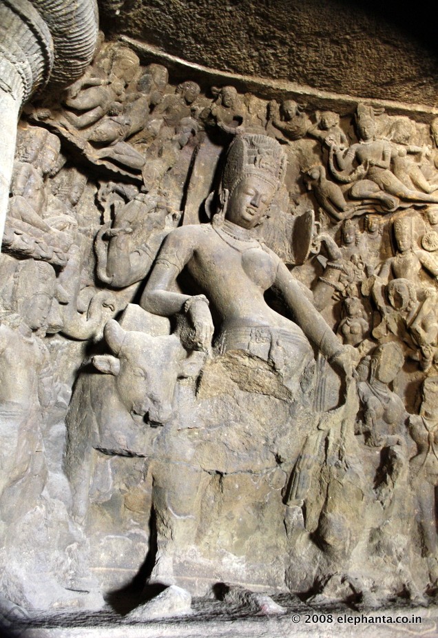 Ardhanarishvara at Elephanta . The image depicts the Parvathi's side. Note the elaborate crown decoration. Seen on the left standing is Kumara (Kartikeya), the Lord of War and above him seen seated on lotus flower is Brahma , the Lord of Creation.